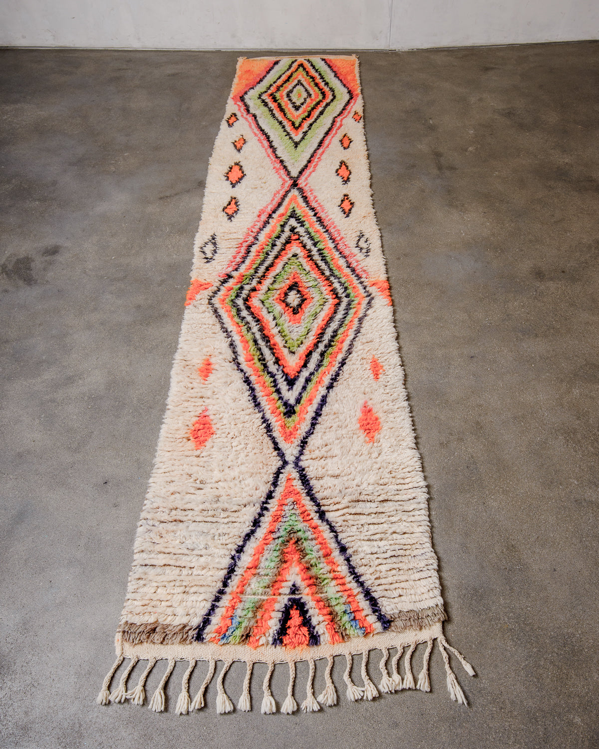 Berberlin vintage runner rug made of cream and brightly coloured wool, laying flat on concrete floor.